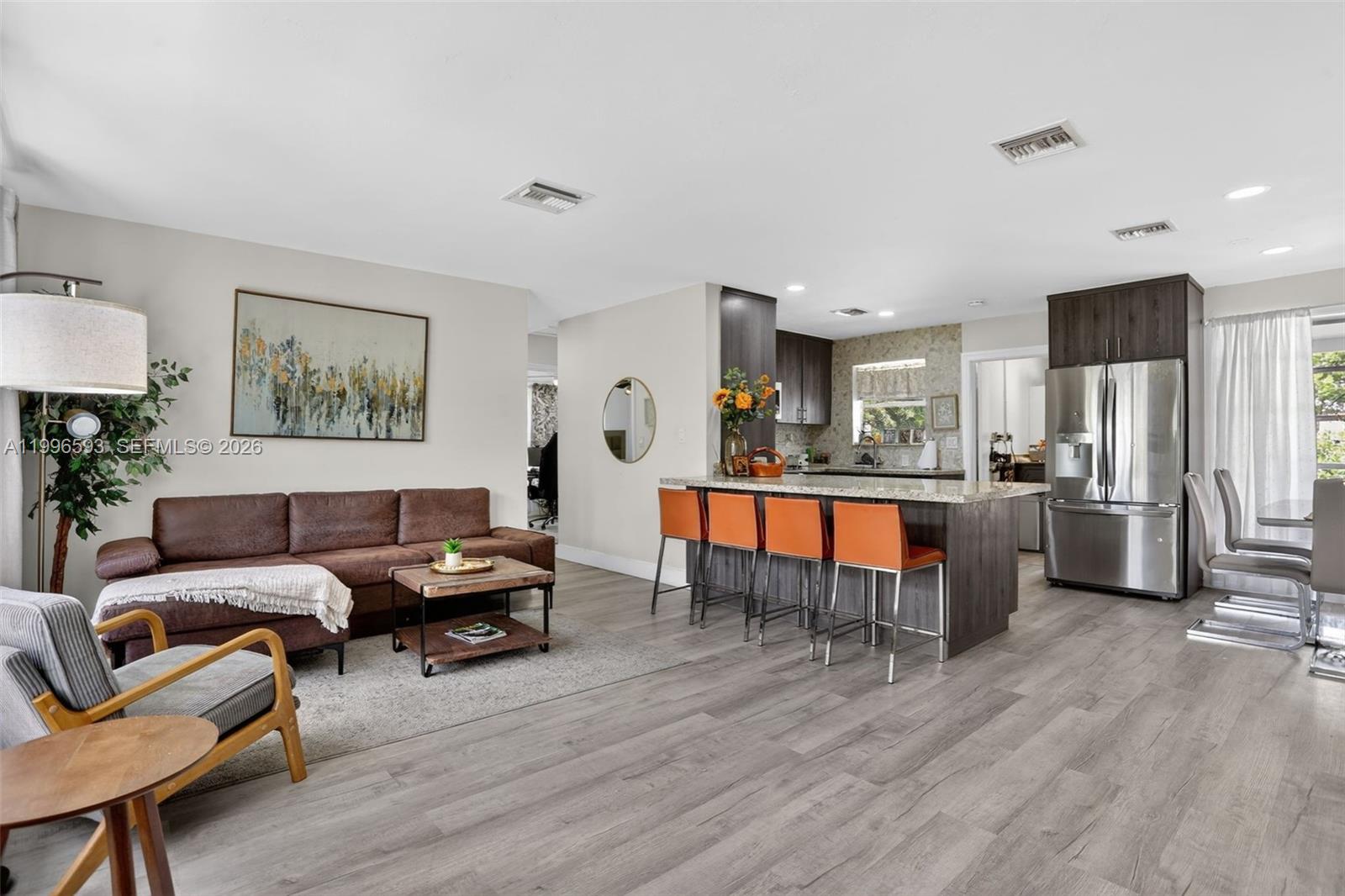 An open-concept living room and kitchen feature wood-look flooring, a brown sofa, and orange barstools — 1357 SW 4th Ter, Pompano Beach FL 33060, POMPANO BEACH, FL