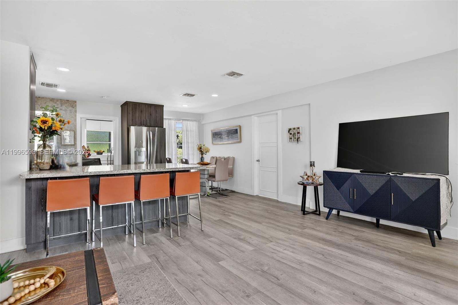 An open-concept living area features a kitchen island with orange stools and wood flooring — 1357 SW 4th Ter, Pompano Beach FL 33060, POMPANO BEACH, FL