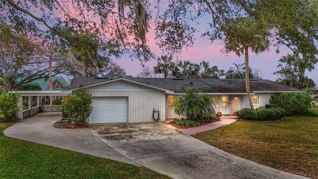 A single-story white brick house with a garage, carport, and a paved walkway at dusk — 803 N SHORE DRIVE, LEESBURG, FL