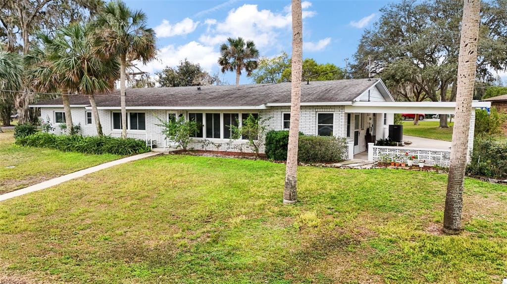 A single-story white brick house with a carport and palm trees in the front yard — 803 N SHORE DRIVE, LEESBURG, FL
