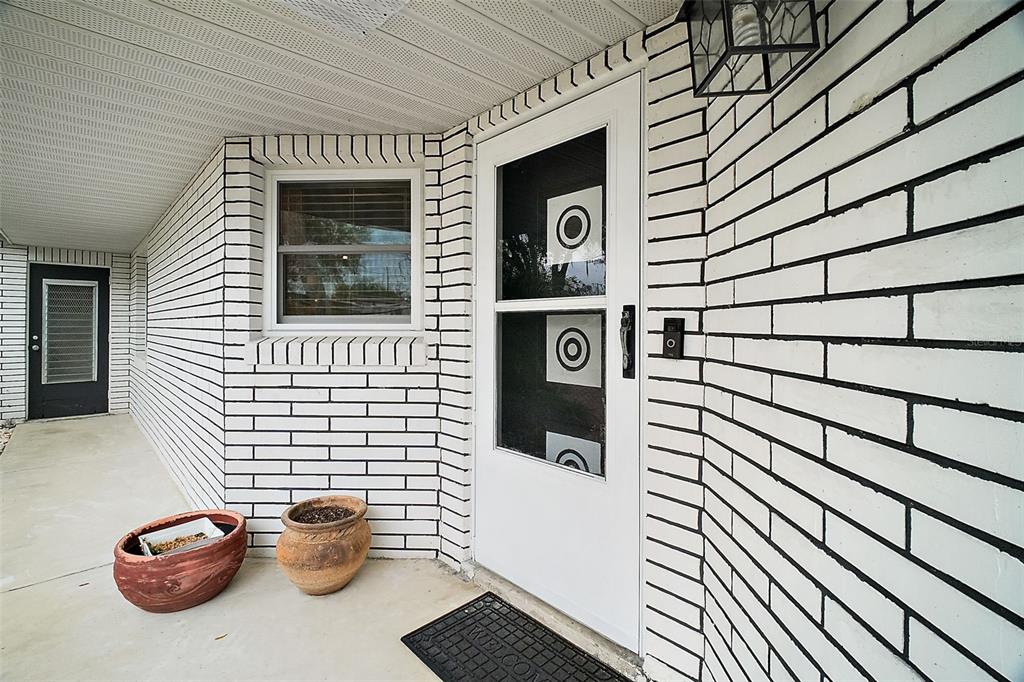 A white brick exterior wall features a front door with a storm door and window — 803 N SHORE DRIVE, LEESBURG, FL
