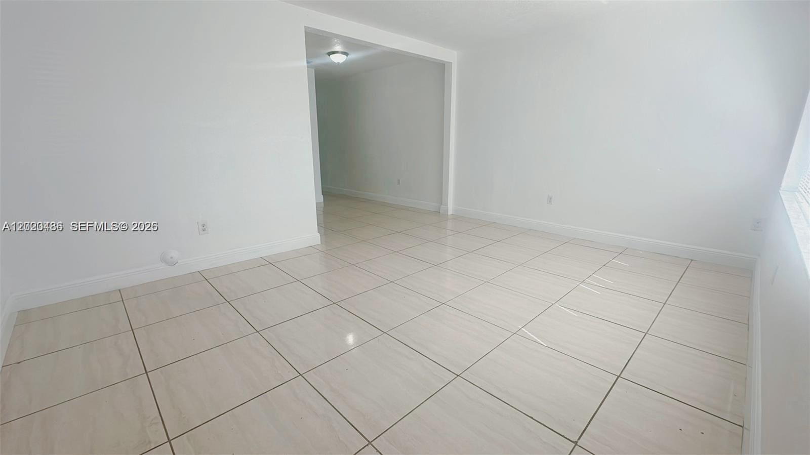 An empty room features white walls, light-colored tile flooring, a large window, and a door — 2125 NW 66th St # 2, Miami FL 33147, MIAMI, FL