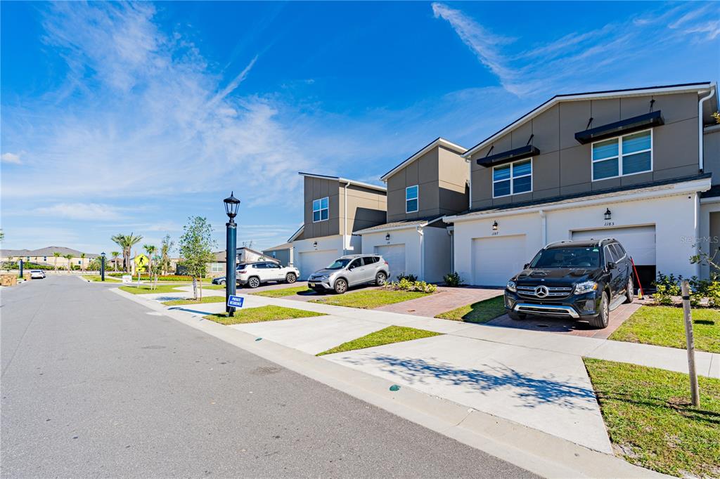 A row of modern townhomes with attached garages and driveways under a bright blue sky — 1187 BOARDWALK PLACE, KISSIMMEE, FL