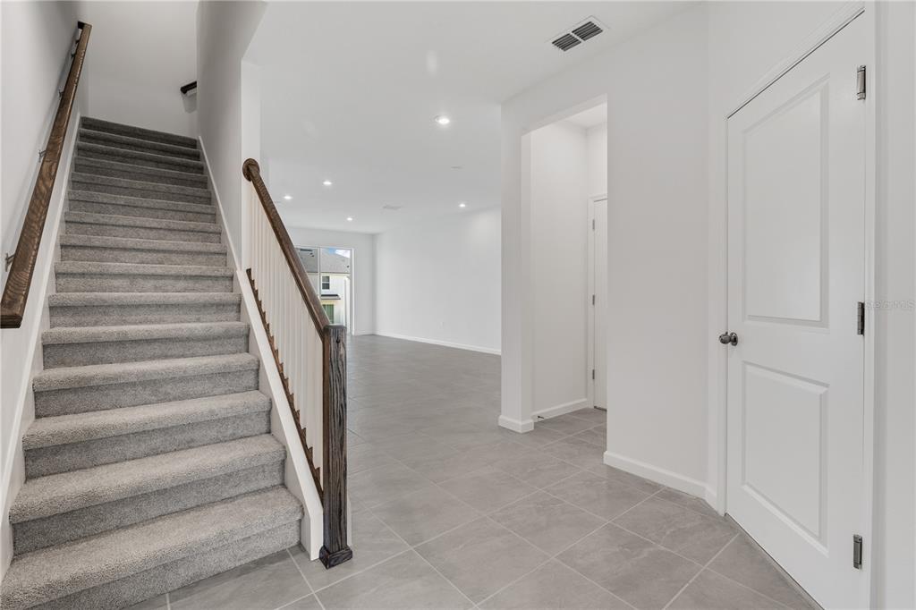 A carpeted staircase with a wooden railing leads to an open living area with tile — 1187 BOARDWALK PLACE, KISSIMMEE, FL