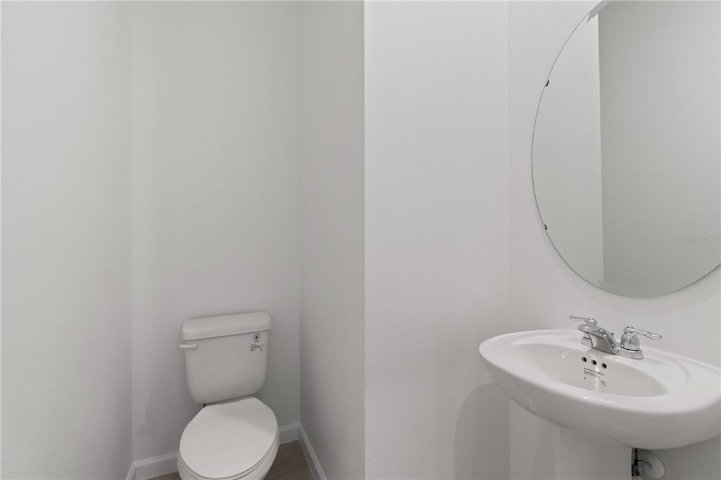 A small bathroom features a white pedestal sink, a round mirror, and a toilet — 1187 BOARDWALK PLACE, KISSIMMEE, FL