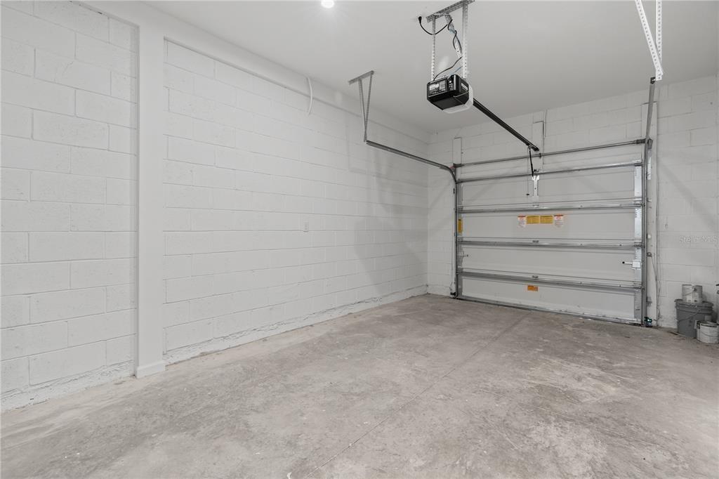 An interior view of a garage with white concrete block walls and a concrete floor — 1187 BOARDWALK PLACE, KISSIMMEE, FL