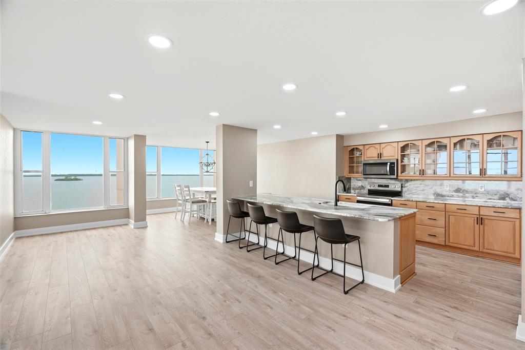 A kitchen with wood cabinets and a breakfast bar overlooks a room with water views — 634 EDGEWATER DRIVE UNIT 844, DUNEDIN, FL