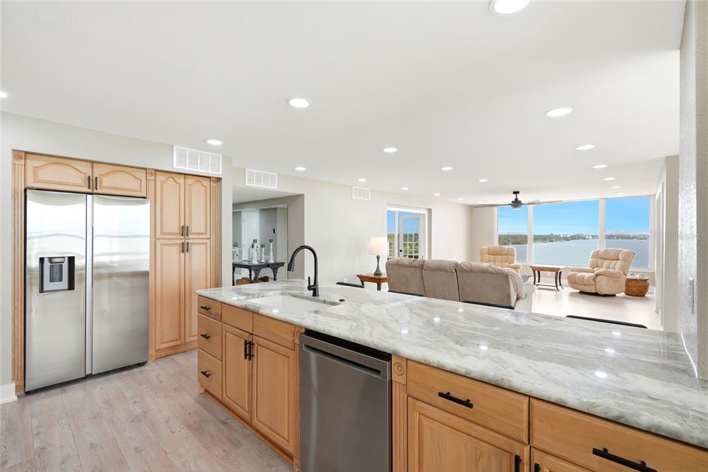 A kitchen with light wood cabinets, stone countertops, and stainless steel appliances overlooks a living area — 634 EDGEWATER DRIVE UNIT 844, DUNEDIN, FL
