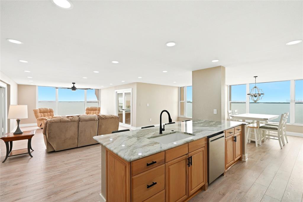 An open-concept kitchen with granite countertops and wood cabinets overlooks a living and dining area — 634 EDGEWATER DRIVE UNIT 844, DUNEDIN, FL