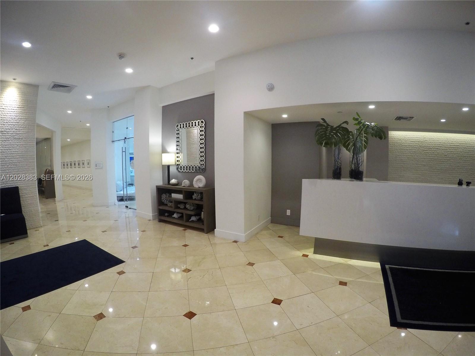 A modern lobby features a white reception desk, tiled floors, and a decorative console table — 100 Lincoln Rd # 602, Miami Beach FL 33139, MIAMI BEACH, FL