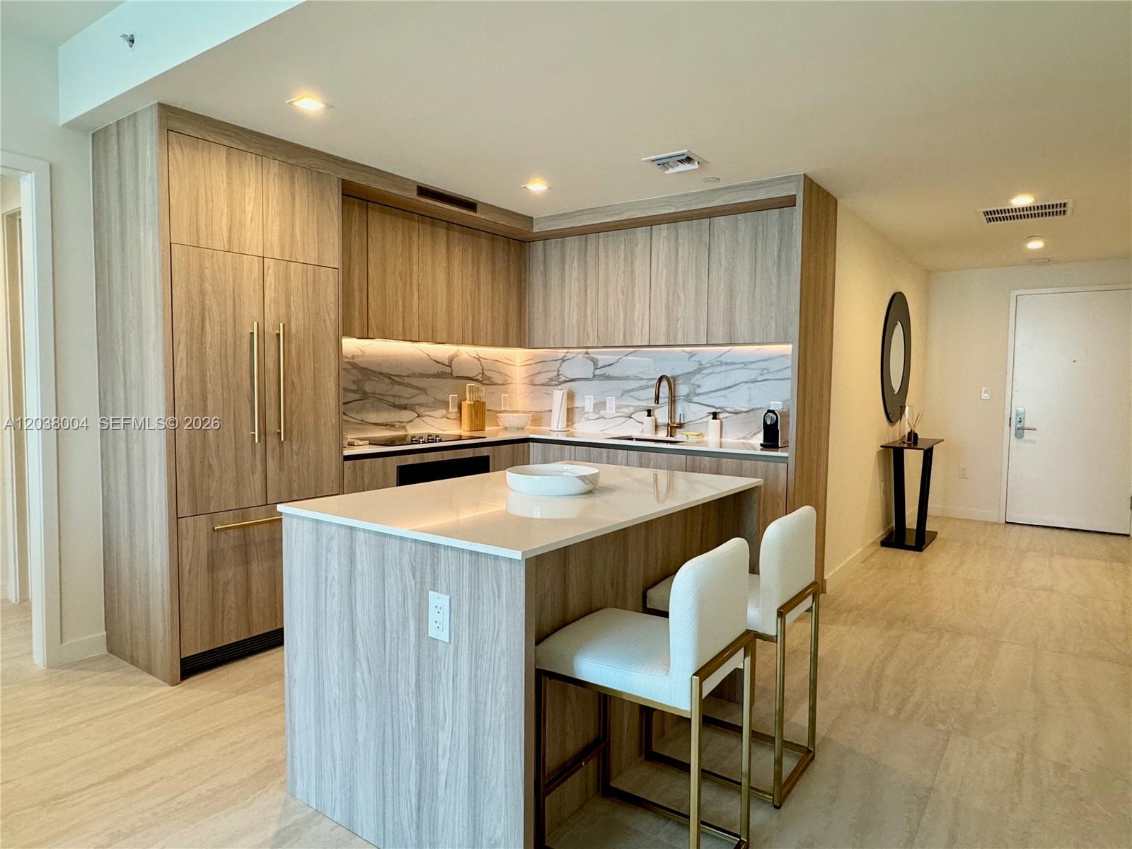 A modern kitchen features wood-grain cabinetry, a marble backsplash, and a central island with seating — 77 SE 5th St # 4002, Miami FL 33131, MIAMI, FL