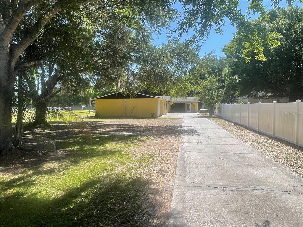A yellow house sits at the end of a long concrete driveway beside a fence — 3575 MICHIGAN AVENUE, ST CLOUD, FL