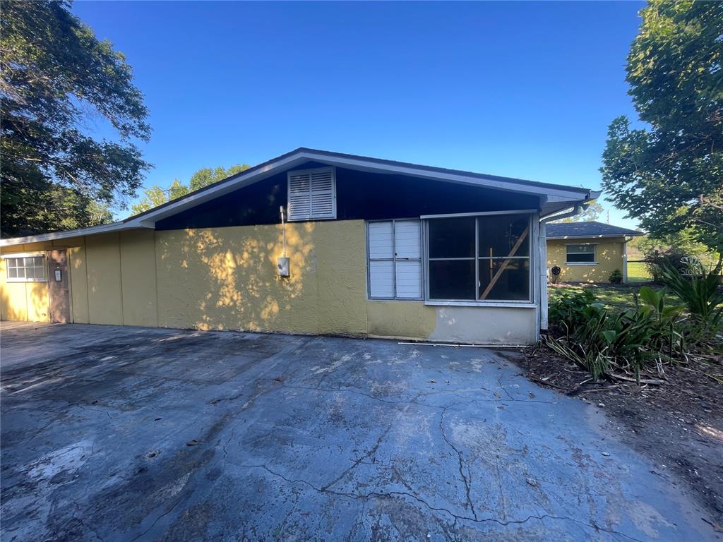 An exterior view of a yellow house with a cracked concrete driveway and large windows — 3575 MICHIGAN AVENUE, ST CLOUD, FL