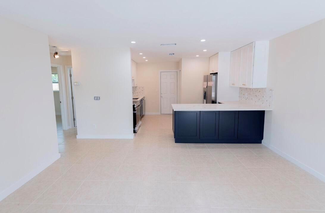 A kitchen features a dark blue island, white upper cabinets, and light-colored tile flooring — 1867 Windsor Drive, North Palm Beach FL 33408, NORTH PALM BEACH, FL