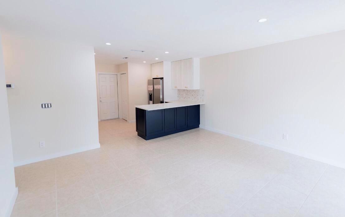 A bright, open-concept kitchen features dark blue lower cabinets, white upper cabinets, and tile flooring — 1867 Windsor Drive, North Palm Beach FL 33408, NORTH PALM BEACH, FL