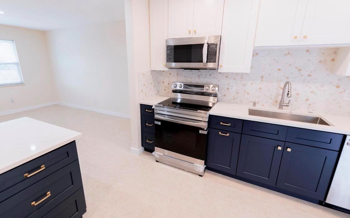 A kitchen features navy blue lower cabinets, white upper cabinets, stainless steel appliances, and quartz countertops — 1867 Windsor Drive, North Palm Beach FL 33408, NORTH PALM BEACH, FL