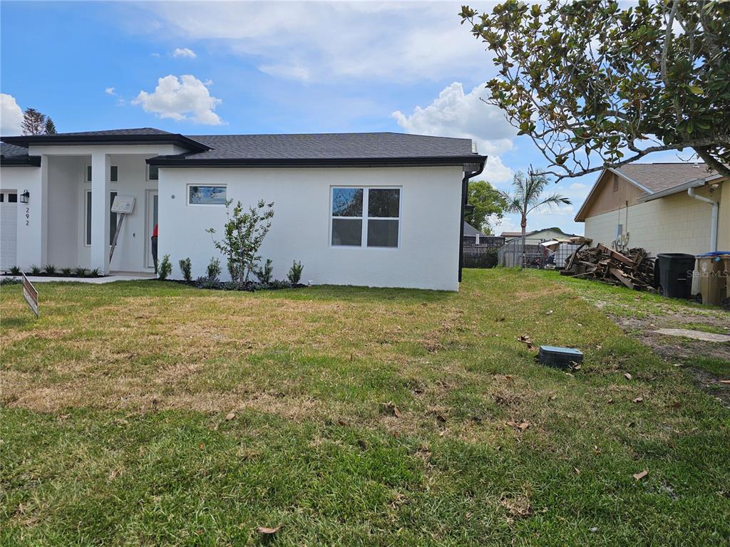 A white house with a dark roof stands next to a neighboring property with debris — 292 GARDENIA ROAD, KISSIMMEE, FL