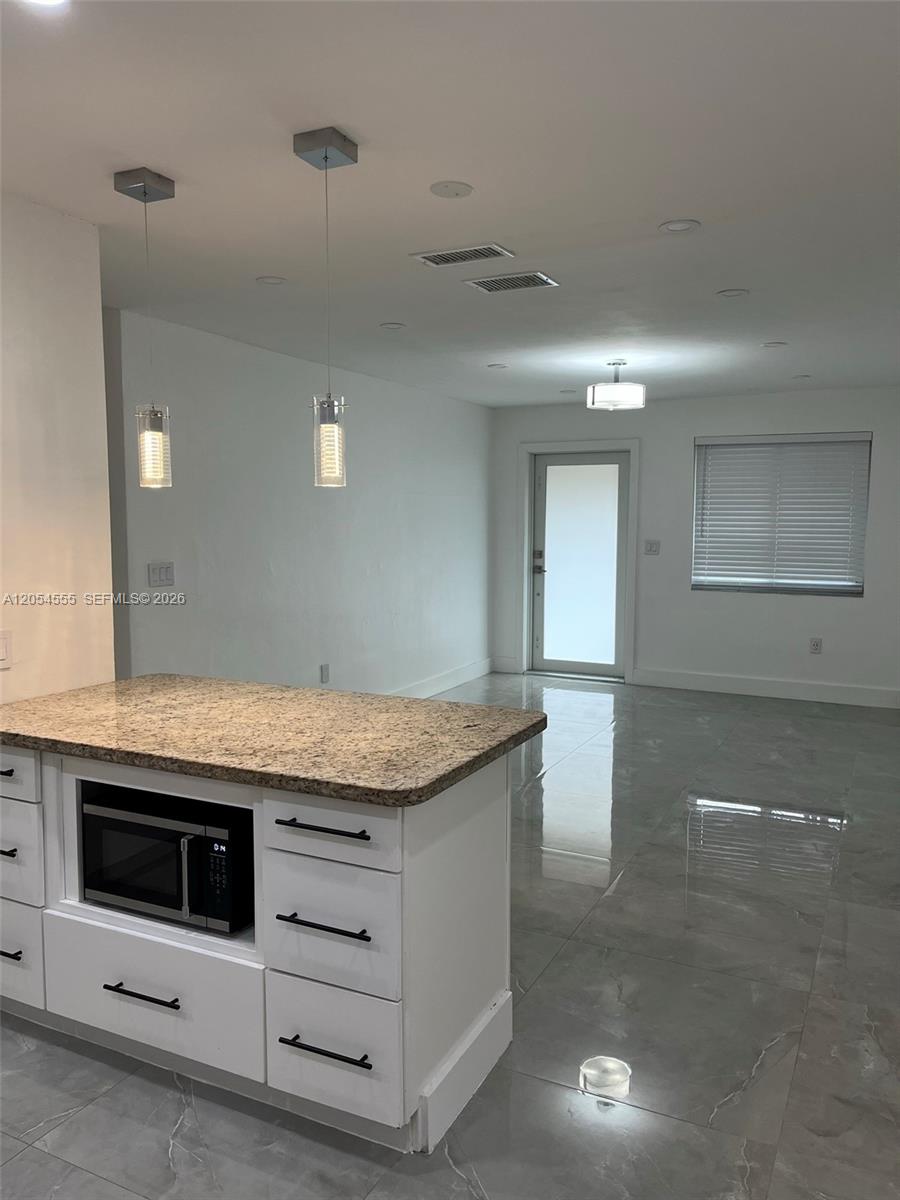 A kitchen island with a granite countertop sits in a room with white cabinets — 2783 SW 33rd Ave # 2783, Miami FL 33133, MIAMI, FL
