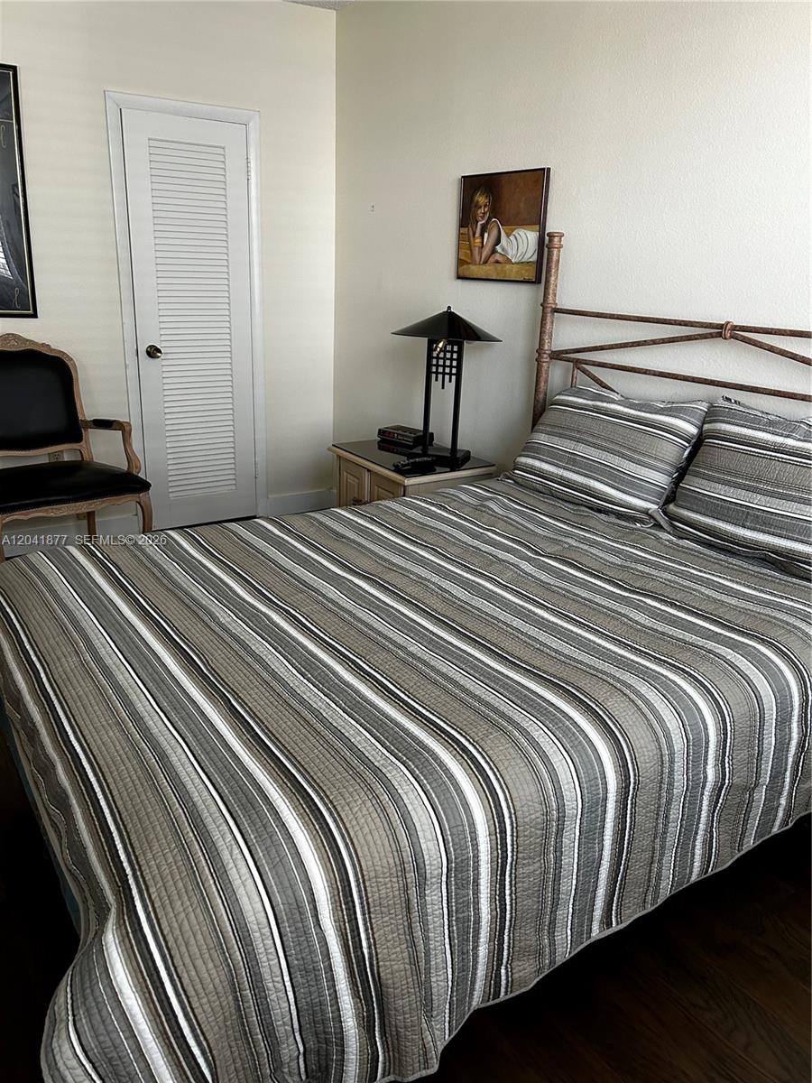 A bedroom features a striped bedspread, a metal headboard, a bedside lamp, and a chair — 1980 S Ocean Dr # 8A, Hallandale Beach FL 33009, HALLANDALE BEACH, FL