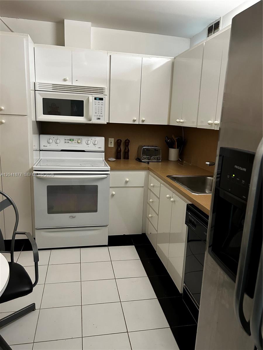A kitchen features white cabinets, white appliances, a tan countertop, and black and white flooring — 1980 S Ocean Dr # 8A, Hallandale Beach FL 33009, HALLANDALE BEACH, FL