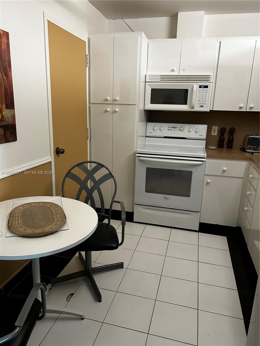 A small kitchen features white cabinets, a white stove, a microwave, and a dining table — 1980 S Ocean Dr # 8A, Hallandale Beach FL 33009, HALLANDALE BEACH, FL