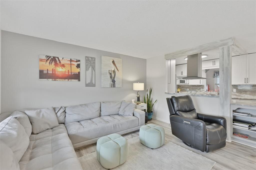A living room features a grey sectional sofa, a black recliner, and a kitchen pass-through — 1739 COCO PALM CIRCLE, SUN CITY CENTER, FL