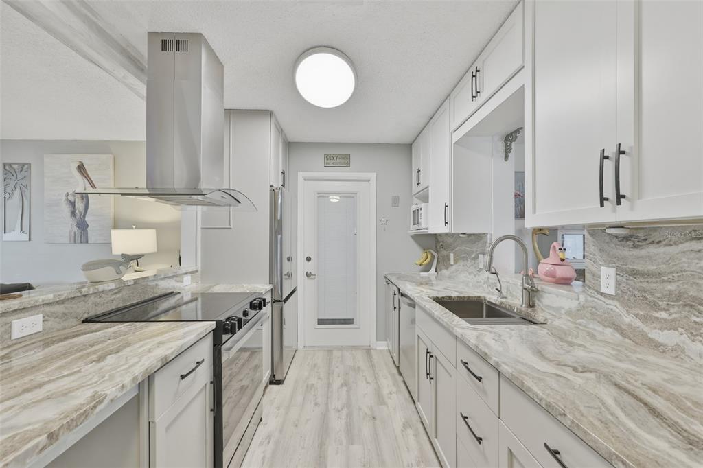 A galley kitchen features white cabinets, marble-patterned countertops, stainless steel appliances, and wood-look flooring — 1739 COCO PALM CIRCLE, SUN CITY CENTER, FL