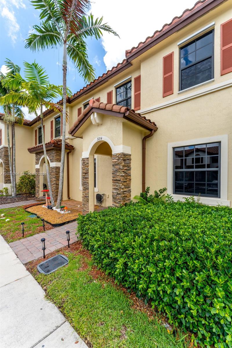 A two-story stucco townhouse features a stone-accented entryway, red tile roof, and landscaped front yard — 3214 SE 4th Ct, Homestead FL 33033, HOMESTEAD, FL