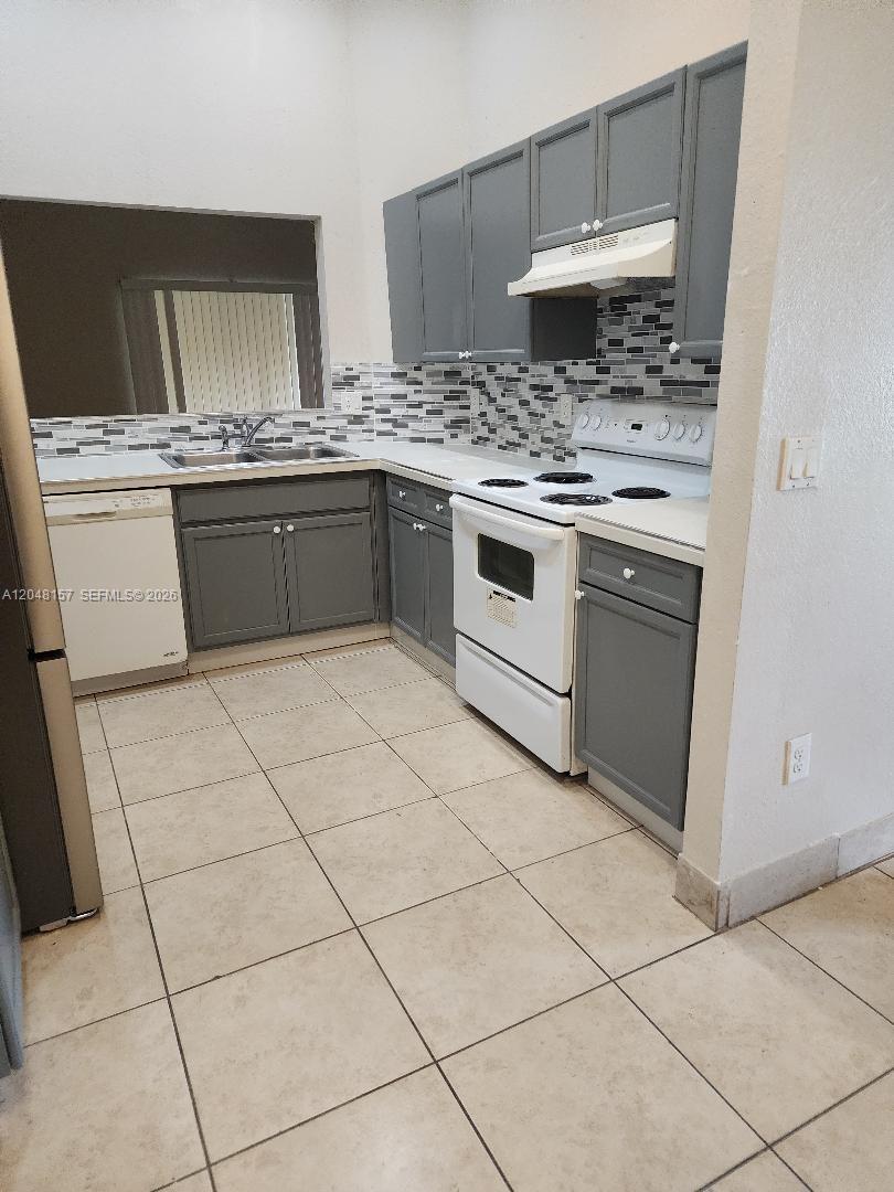 A kitchen features gray cabinets, white appliances, a tiled backsplash, and light-colored floor tiles — 4740 SW 14, Lehigh Acres FL 33973, LEHIGH ACRES, FL