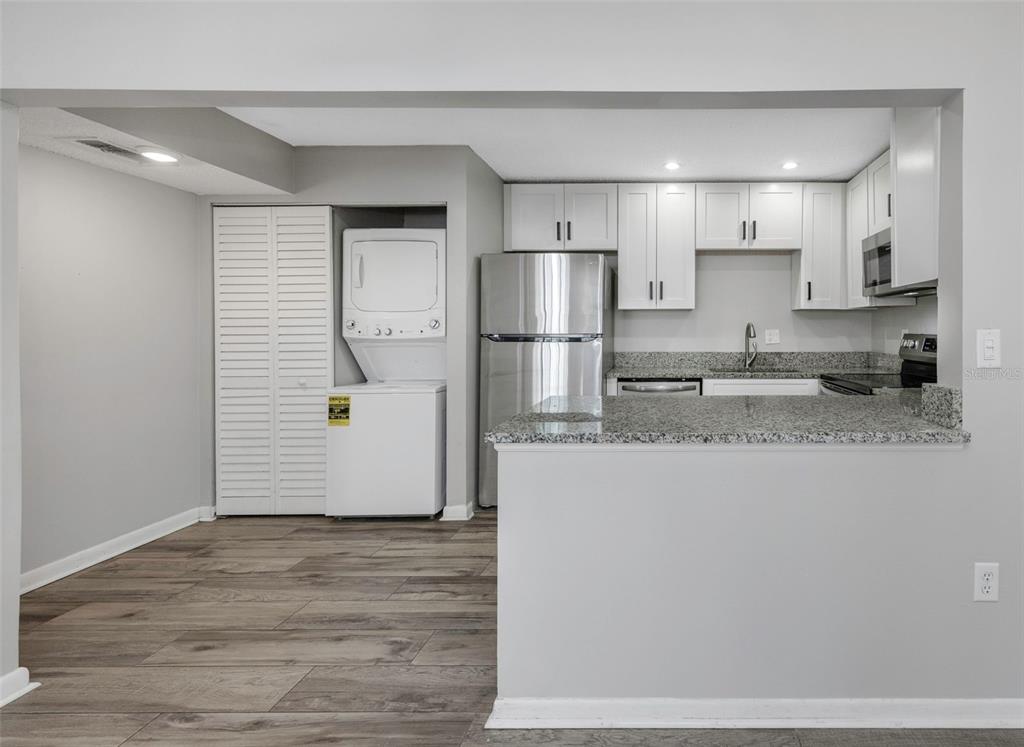 A kitchen with white cabinets, granite countertops, stainless steel appliances, and an adjacent laundry closet — 1281 PINE RIDGE CIRCLE E UNIT A2, TARPON SPRINGS, FL