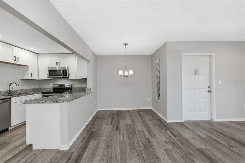 A kitchen with white cabinets and granite countertops opens into a dining area with wood flooring — 1281 PINE RIDGE CIRCLE E UNIT A2, TARPON SPRINGS, FL