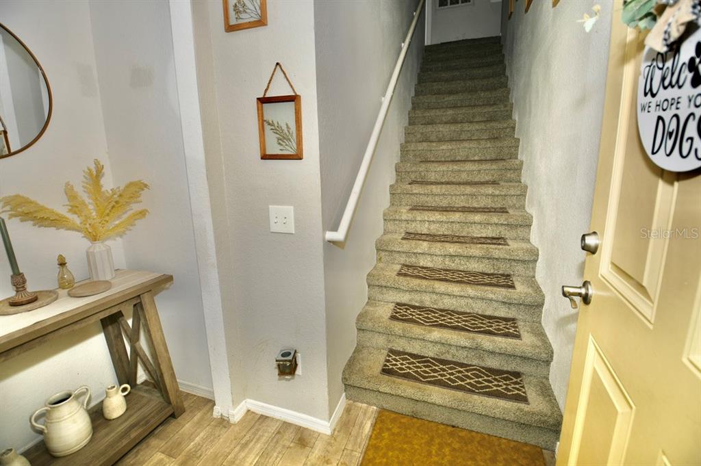 A carpeted staircase with patterned treads leads upward next to a wooden console table — 36121 LAKE CHASE BOULEVARD UNIT 204, ZEPHYRHILLS, FL