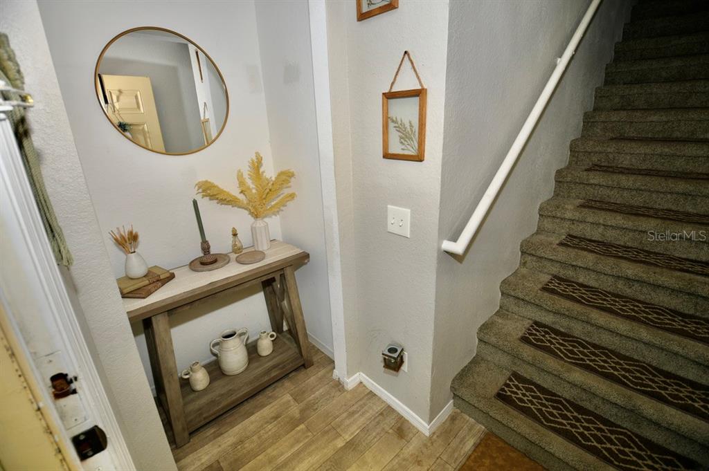 A foyer features a wooden console table, a round mirror, and carpeted stairs with runners — 36121 LAKE CHASE BOULEVARD UNIT 204, ZEPHYRHILLS, FL