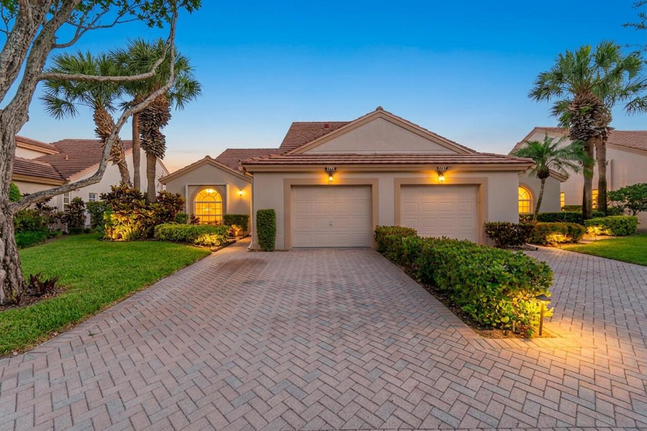 A beige house with a two-car garage and a brick paver driveway at dusk — 7773 Silver Lake Drive, Delray Beach FL 33446, DELRAY BEACH, FL