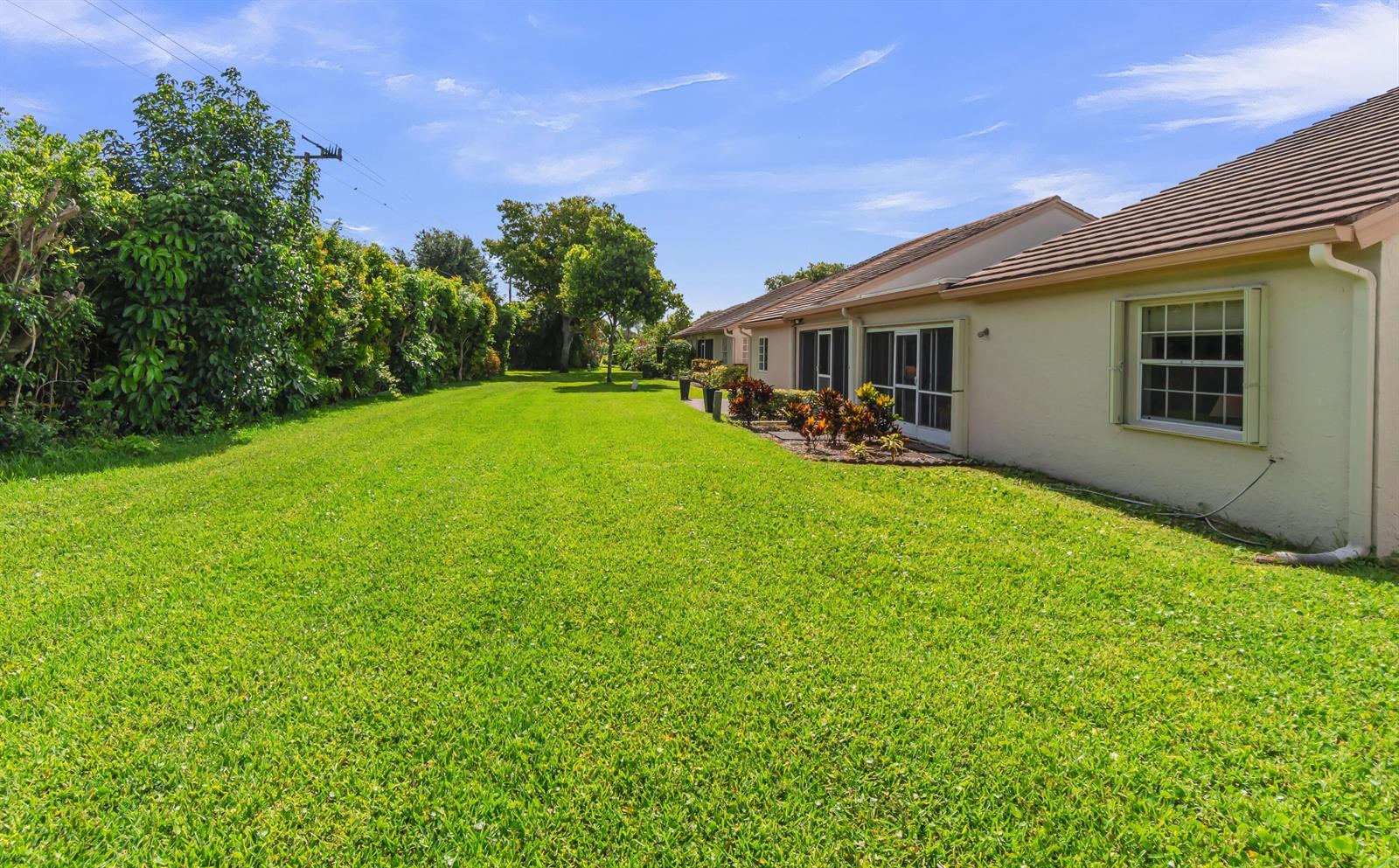A grassy backyard stretches alongside a beige residential building with a tiled roof — 7773 Silver Lake Drive, Delray Beach FL 33446, DELRAY BEACH, FL