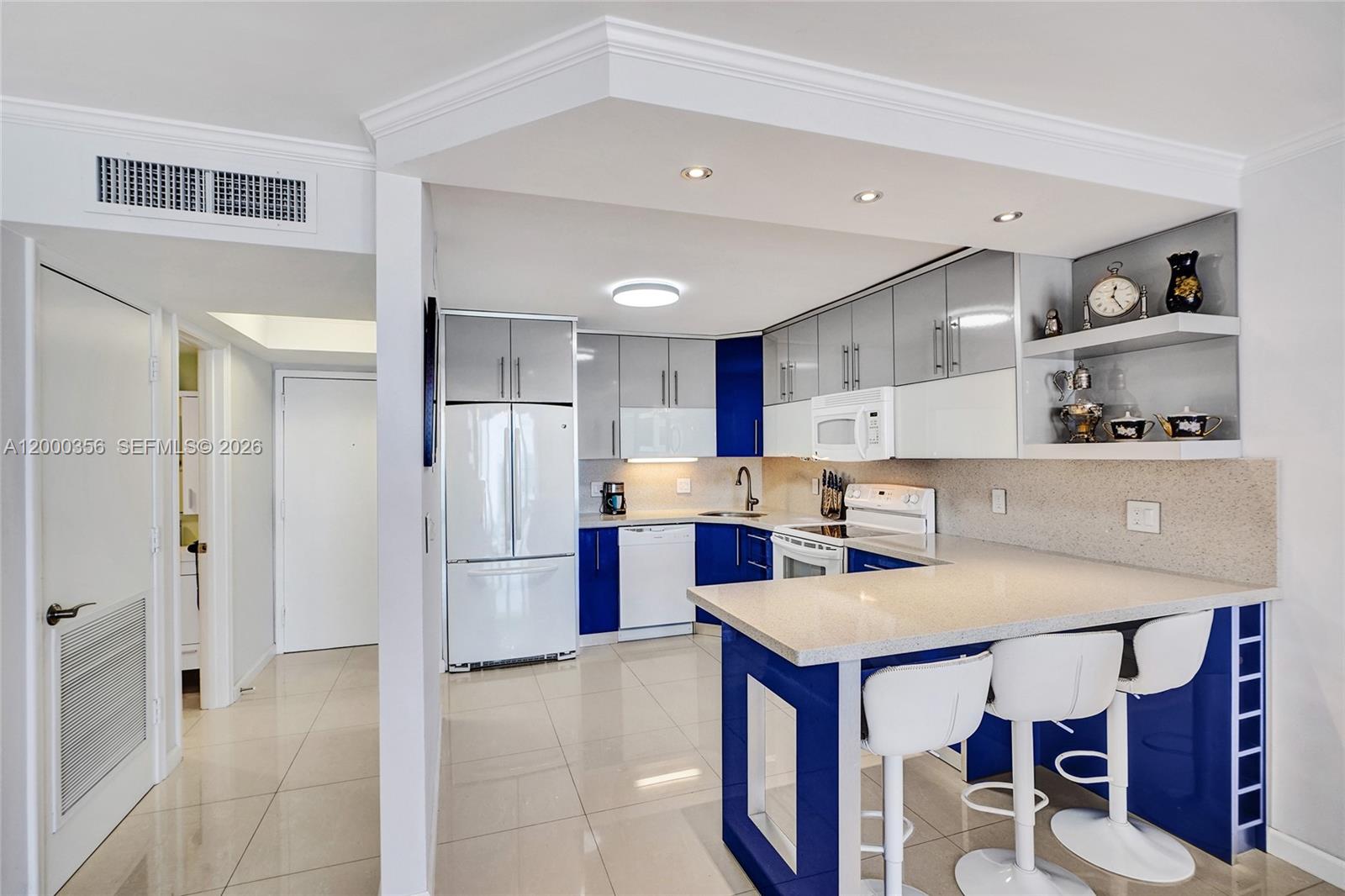 A kitchen features blue and grey cabinetry, white appliances, and a breakfast bar with stools — 2401 S Ocean Dr, Hollywood FL 33019, HOLLYWOOD, FL