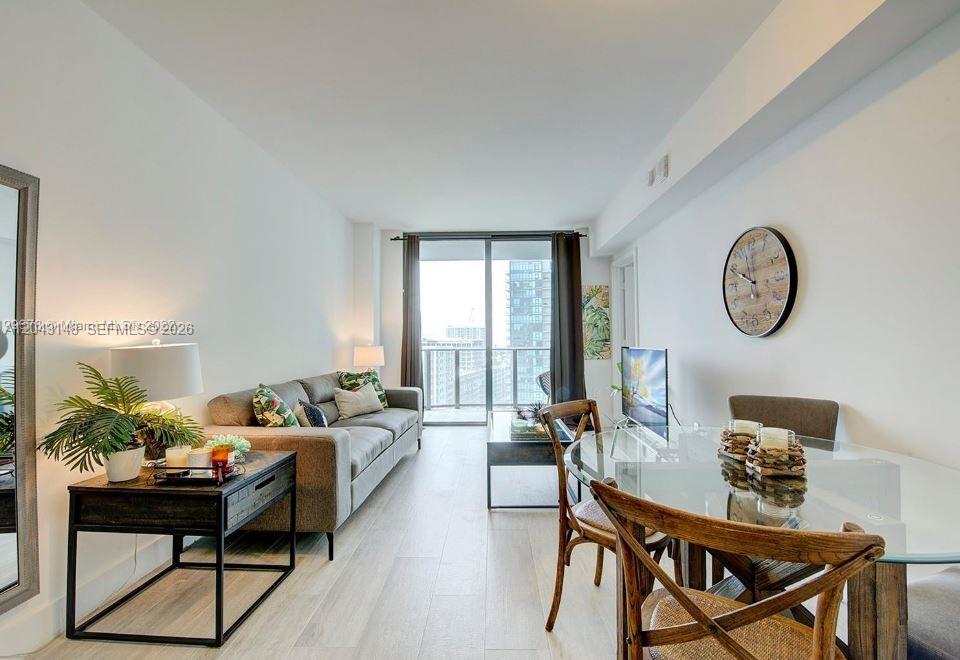 A modern living and dining area features light wood floors, a gray sofa, and balcony access — 121 NE 34th St # 1603, Miami FL 33137, MIAMI, FL