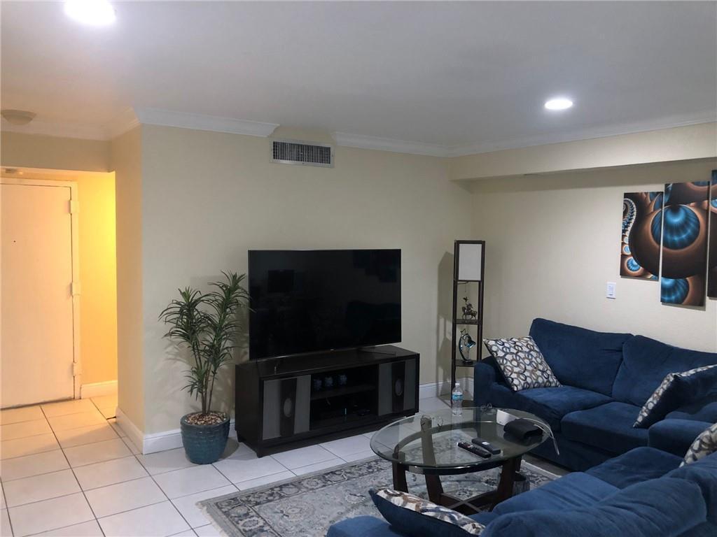 A living room features a large television on a console, a blue sectional, and tile flooring — 10411 N Kendall Drive # B203, Miami FL 33176, MIAMI, FL