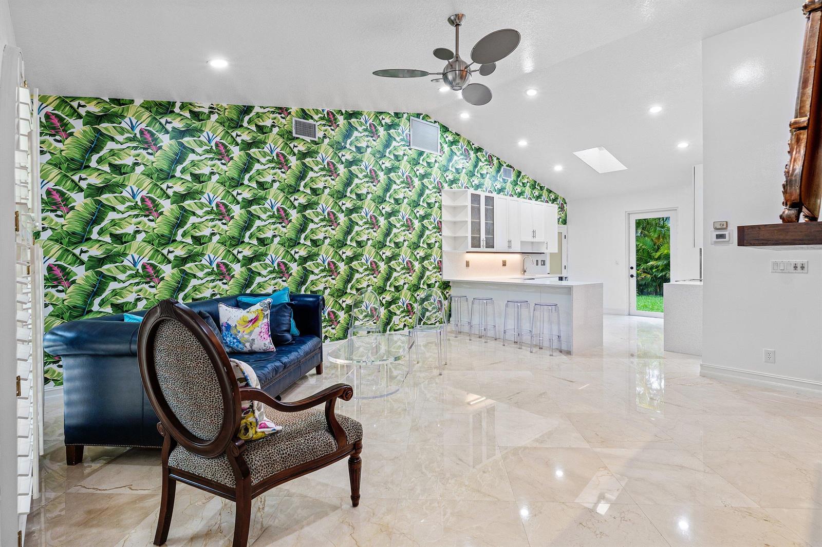A living room with a tropical leaf wallpaper accent wall, blue sofa, and marble flooring — 359 E Ocean Avenue, Lantana FL 33462, LANTANA, FL
