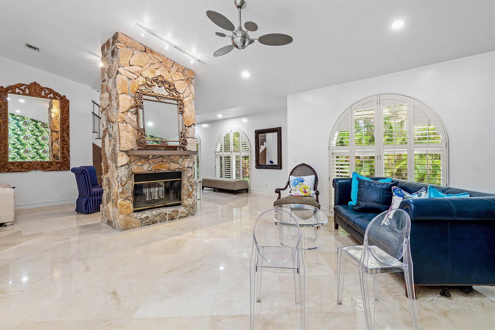 A living room features a stone fireplace, tile floors, a blue sofa, and arched windows — 359 E Ocean Avenue, Lantana FL 33462, LANTANA, FL