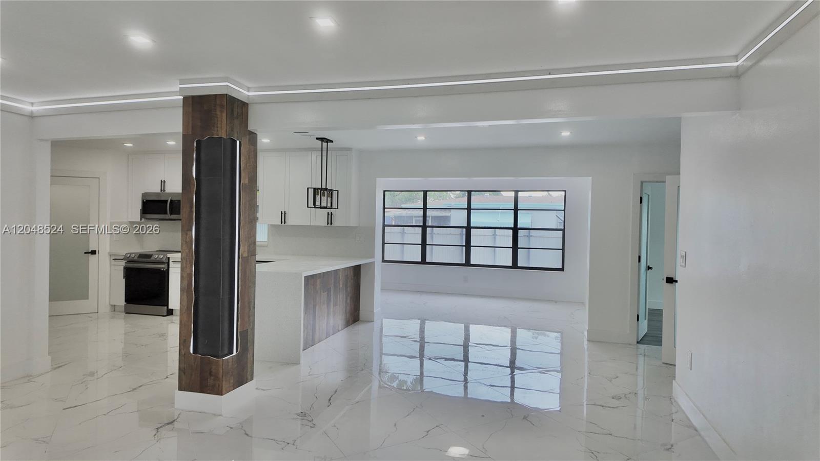 A modern kitchen and living area feature white marble floors and a wood-paneled support column — 7721 Granada Blvd, Miramar FL 33023, MIRAMAR, FL