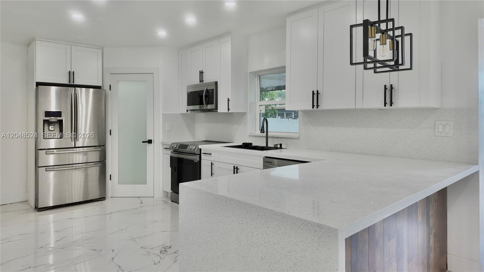 A modern kitchen features white cabinets, stainless steel appliances, and a white quartz waterfall island — 7721 Granada Blvd, Miramar FL 33023, MIRAMAR, FL