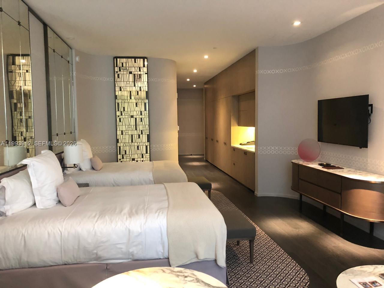A modern hotel room features two beds, a wall-mounted television, and light wood cabinetry — 801 S Miami Ave # 412, Miami FL 33131, MIAMI, FL