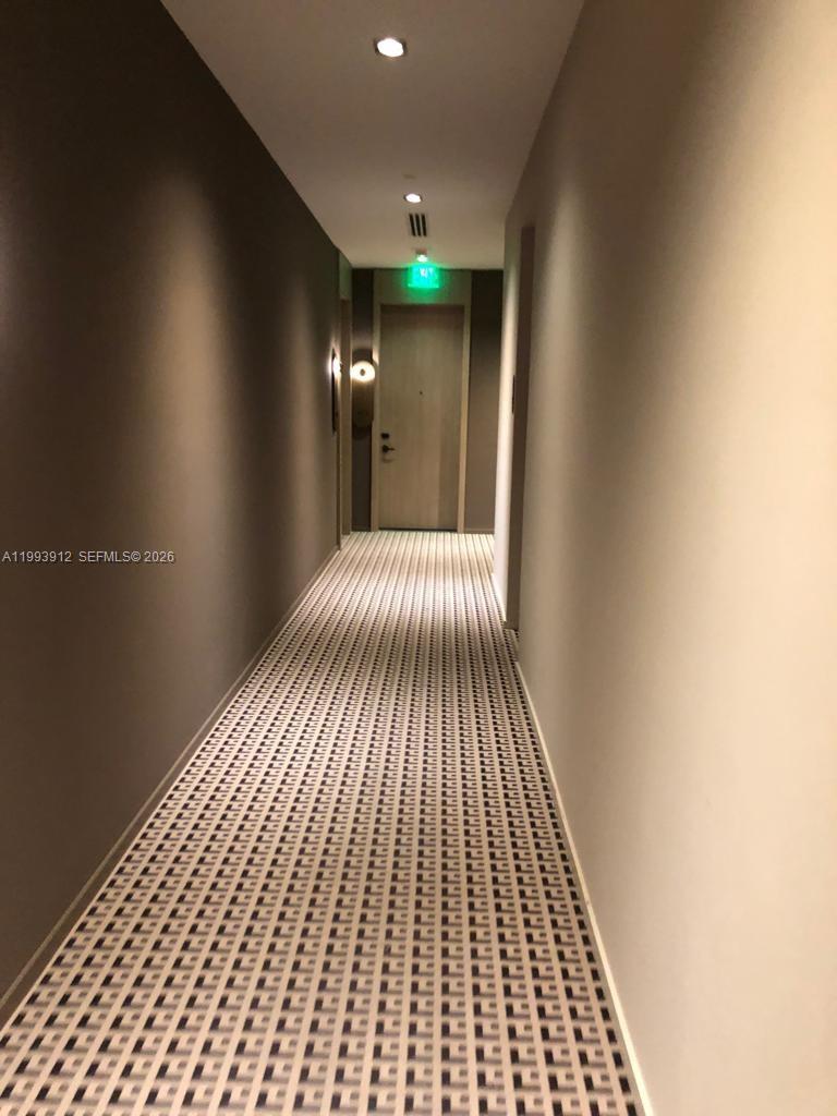 A long, narrow hotel-style hallway features patterned carpeting and a door with an exit sign — 801 S Miami Ave # 412, Miami FL 33131, MIAMI, FL