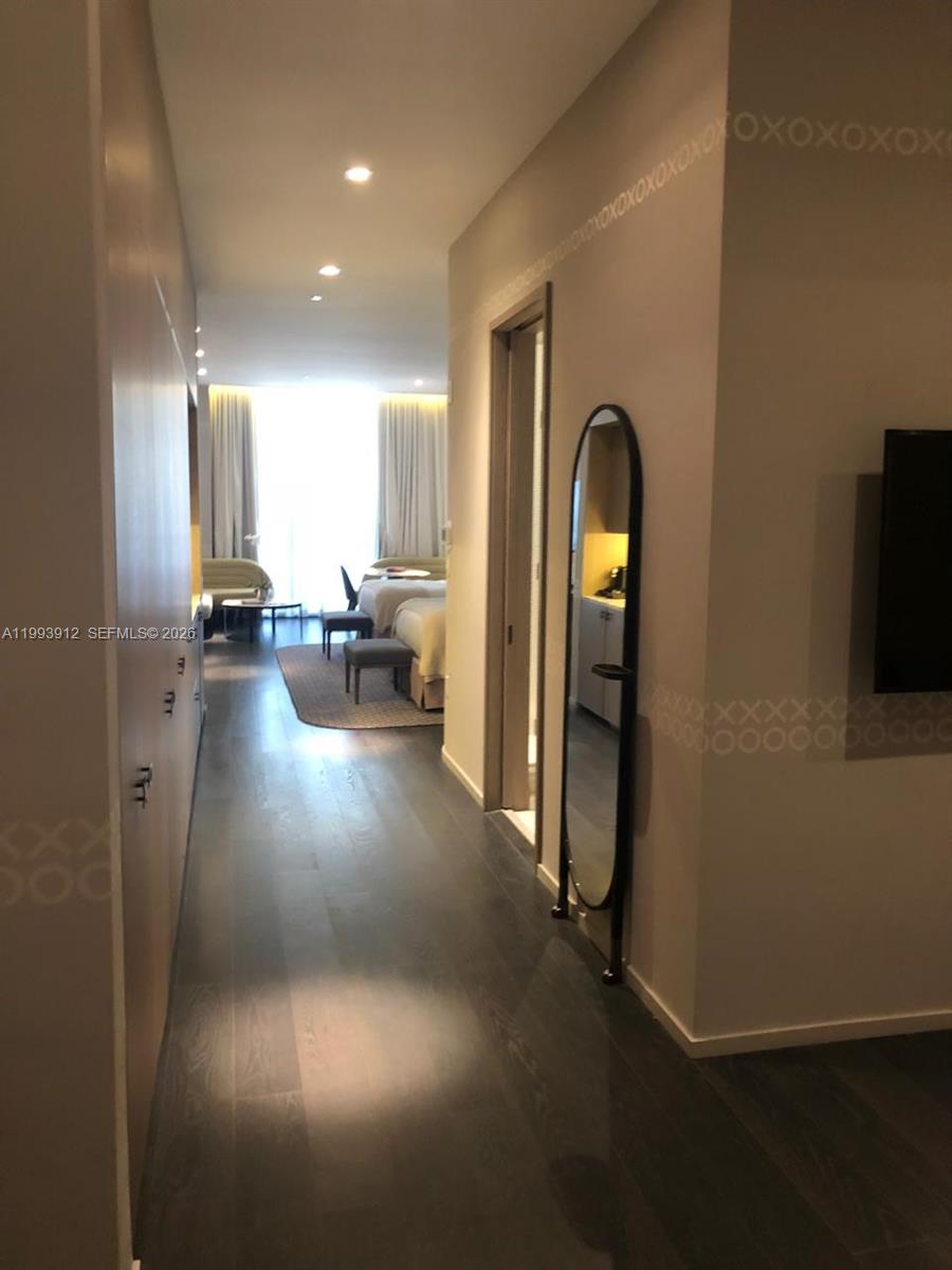 A hallway with dark wood floors leads to a bedroom featuring two beds and curtains — 801 S Miami Ave # 412, Miami FL 33131, MIAMI, FL