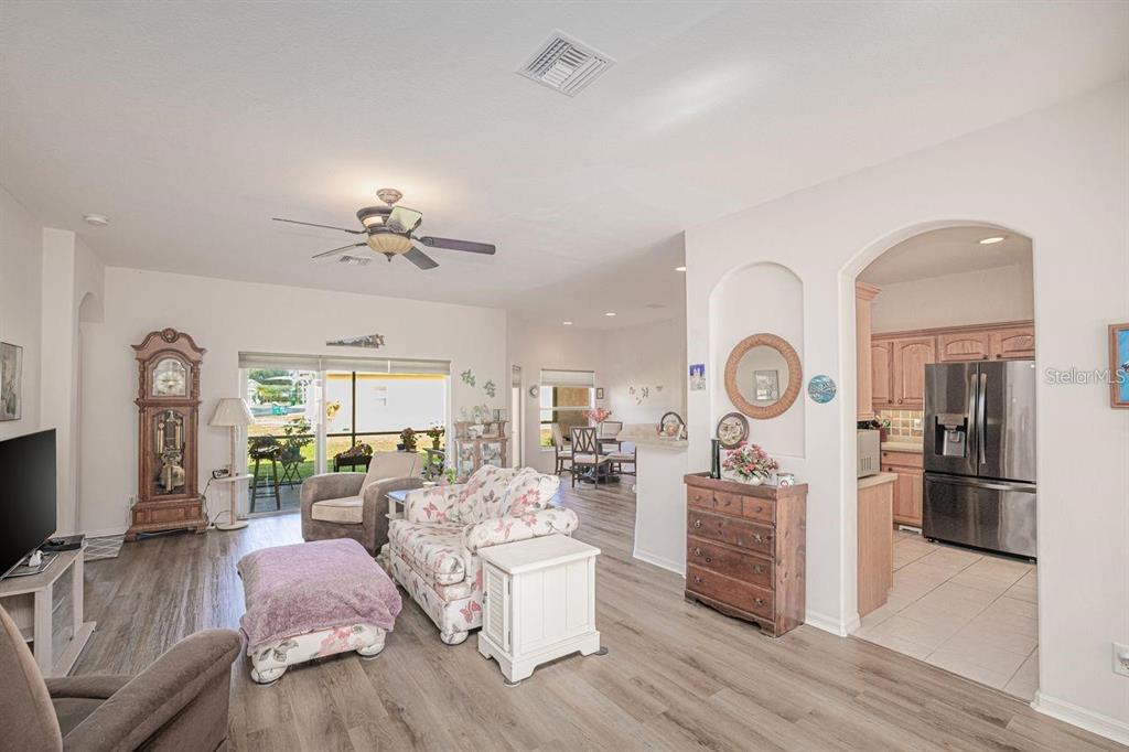 A living room with wood-look flooring, a floral sofa, a grandfather clock, and an adjacent kitchen — 2860 SUNCOAST LAKES BOULEVARD, PORT CHARLOTTE, FL