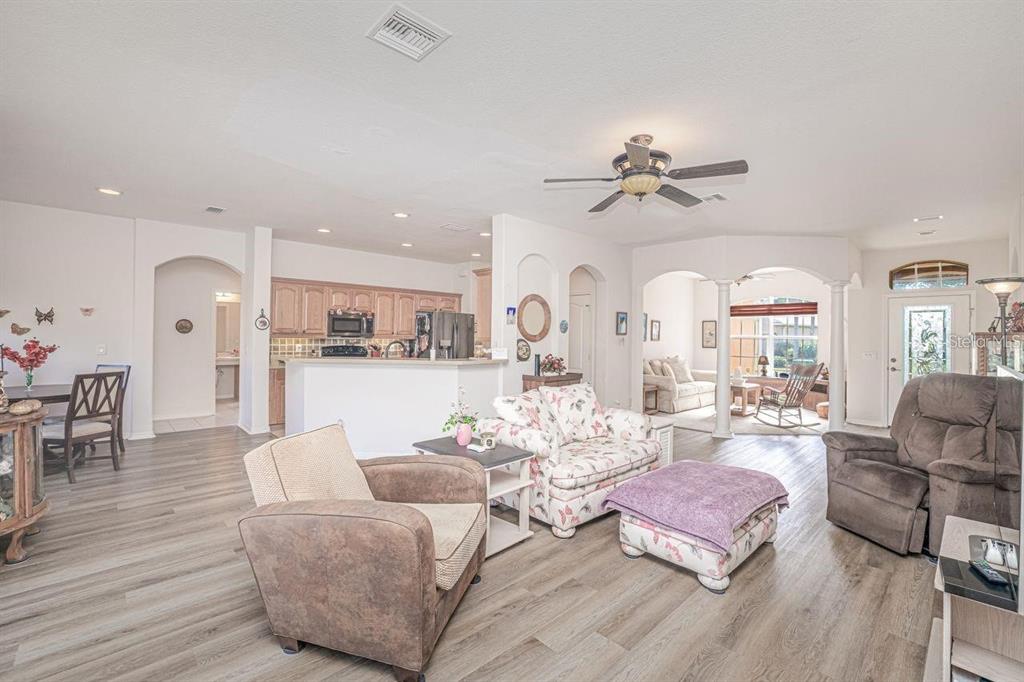 An open-concept living room with light wood-look flooring, a floral sofa, and a kitchen area — 2860 SUNCOAST LAKES BOULEVARD, PORT CHARLOTTE, FL