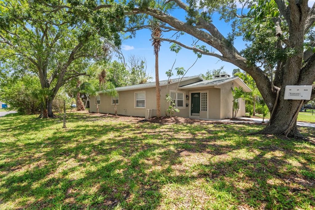A single-story tan house with a dark front door sits on a grassy, tree-filled lot — 4247 HELENA STREET NE, ST PETERSBURG, FL