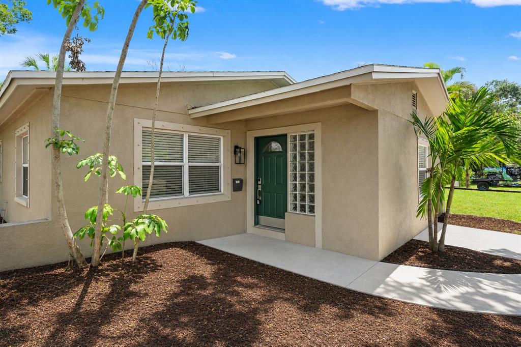 A tan stucco house features a green front door and a glass block window — 4247 HELENA STREET NE, ST PETERSBURG, FL