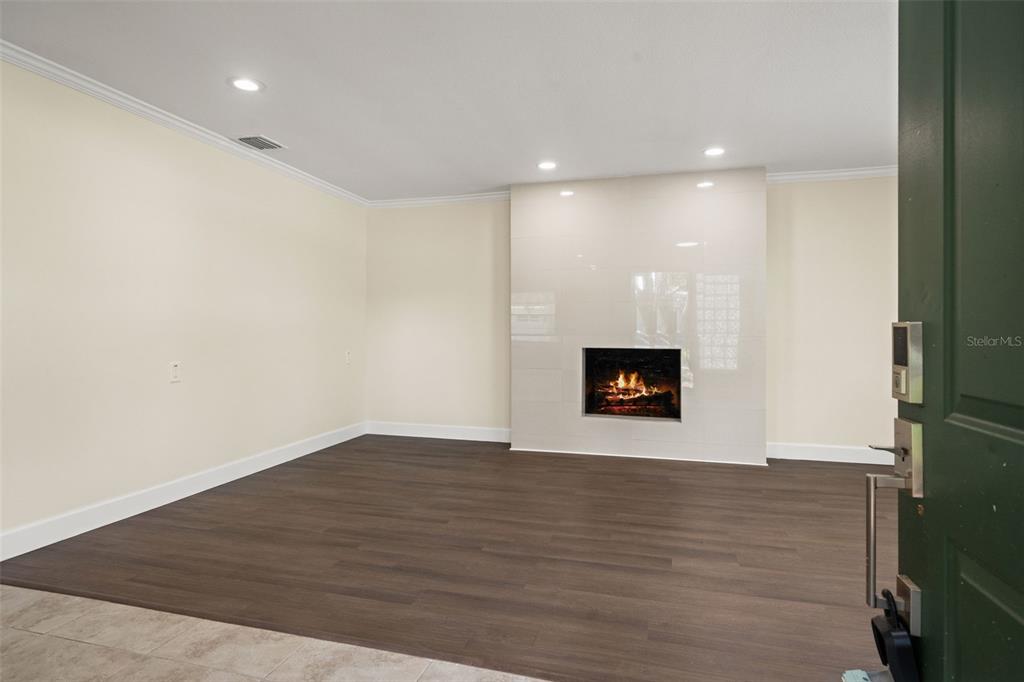 A living room features dark wood-look flooring, cream walls, and a modern tiled fireplace — 4247 HELENA STREET NE, ST PETERSBURG, FL